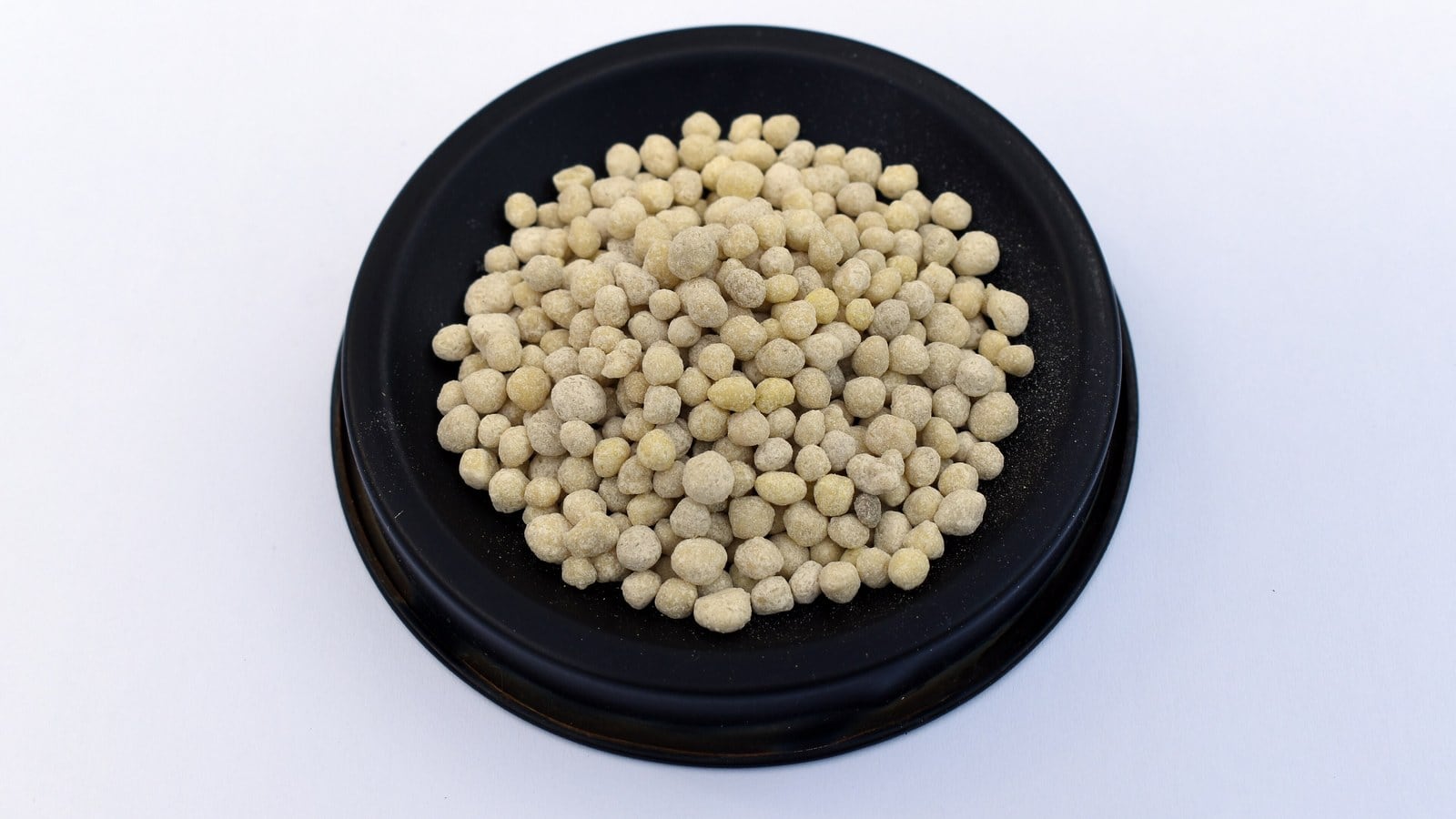 A dish of pale granular fertiliser on a white background